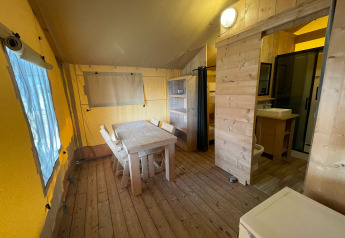 Indersiden af et safari telt med træmøbler, spisebord, køkken og badeværelse i Glamping Klein Strand.