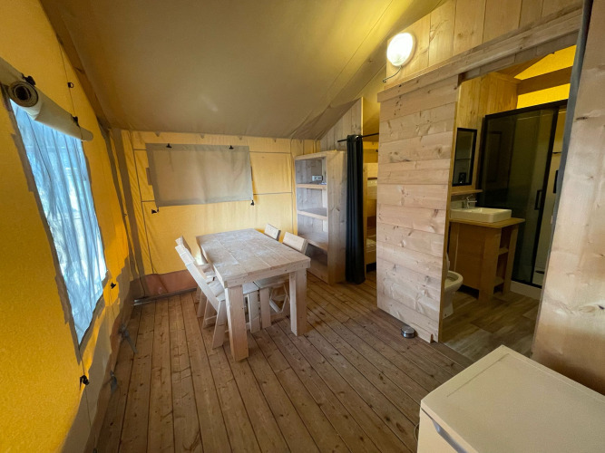 Interieur van een safaritent met houten meubels, eettafel, keuken en badkamer bij Glamping Klein Strand.