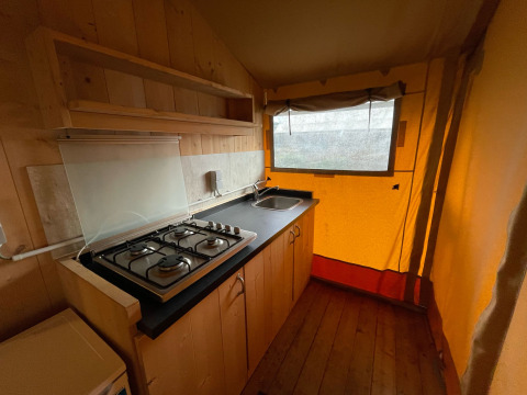 Área de cocina en una tienda safari de Glamping en Vakantiepark Klein Strand, Bélgica, con estufa y fregadero.