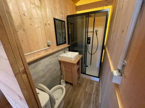 Modern bathroom with wood walls, shower, toilet, and sink in a glamping safari tent in Belgium.