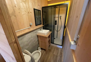 Modern bathroom with wood walls, shower, toilet, and sink in a glamping safari tent in Belgium.