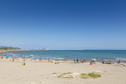 Strandbillede med folk, der solbader og svømmer ved Camping Vilanova Park i Catalonien, Spanien.
