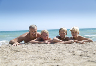 Famiglia sdraiata sulla sabbia al Camping Vilanova Park in Catalogna, Spagna, con il mare sullo sfondo.