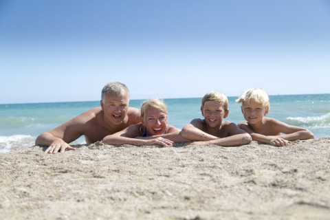 Familia tumbada en la arena en Camping Vilanova Park, Cataluña, España, con el mar de fondo.