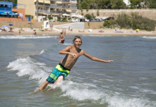 Ragazzo gioca in mare vicino alla spiaggia a Camping Vilanova Park, villaggio turistico in Catalogna, Spagna, estate.