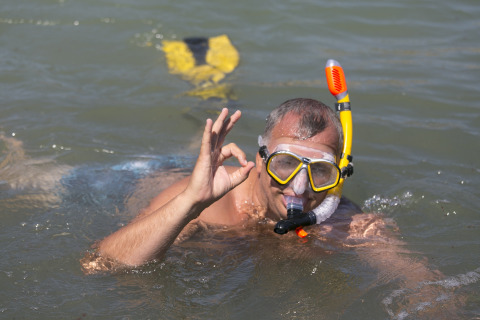 Uomo che fa snorkeling in mare con attrezzatura gialla, fa OK al Camping Vilanova Park, Catalogna, Spagna.