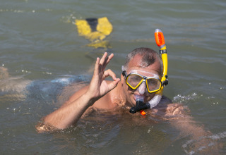 Man snorkelt in zee met gele uitrusting en geeft OK-teken, Camping Vilanova Park, Catalonië, Spanje.