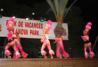 Dancers in vibrant pink costumes perform on stage at night at Camping Vilanova Park in Catalonia, Spain.
