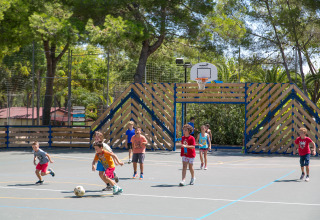 Bambini che giocano a calcio su un campo da basket all’aperto al Camping Vilanova Park tra gli alberi.