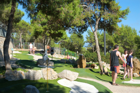 Familias juegan al minigolf entre árboles en Camping Vilanova Park, un parque vacacional en Cataluña, España.