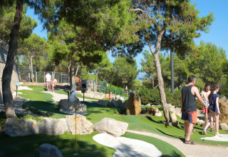 Famiglie si divertono a minigolf tra gli alberi al Camping Vilanova Park, parco vacanze in Catalogna, Spagna.