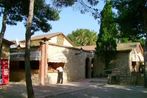 Stone building bar and restaurant with trees and palms at Vilanova Park holiday park in Catalonia, Spain.