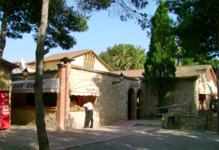 Bar e ristorante in pietra con alberi e palme al campeggio Vilanova Park in Catalogna, Spagna.