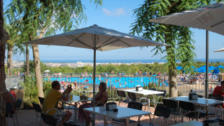 Vista desde la terraza del café en Camping Vilanova Park, Cataluña, España, con piscina y mar al fondo.