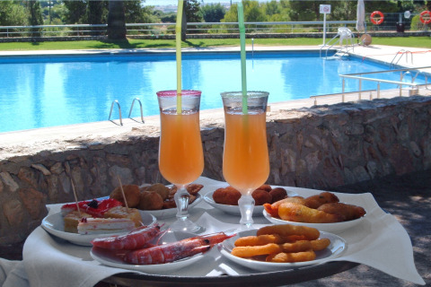 Poolside bord med forfriskende drinks, rejer, småkager og tapas på Camping Vilanova Park i Catalonien, Spanien.