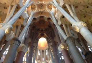 Interior view of the Sagrada Família in Barcelona, showing columns and the ornate ceiling above.