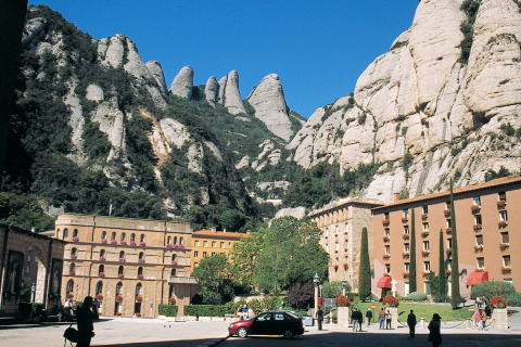 Historic buildings with tourists in front of stunning mountains at Camping Vilanova Park in Catalonia, Spain.