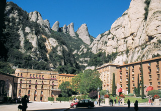 Historic buildings with tourists in front of stunning mountains at Camping Vilanova Park in Catalonia, Spain.