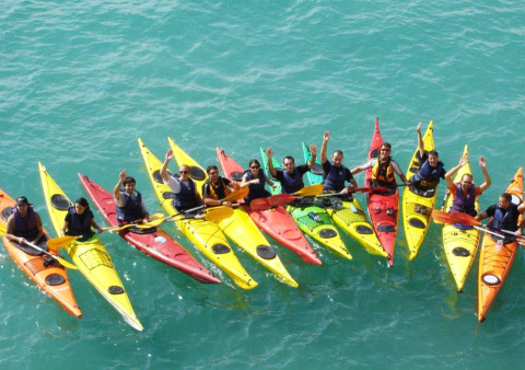 A group of people in colorful kayaks gathers on blue water at Camping Vilanova Park in Catalonia, Spain.