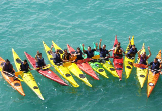 A group of people in colorful kayaks gathers on blue water at Camping Vilanova Park in Catalonia, Spain.
