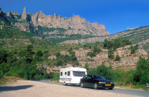 Black car towing a caravan on a scenic mountain road near Camping Vilanova Park in Catalonia, Spain.
