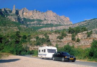 Black car towing a caravan on a scenic mountain road near Camping Vilanova Park in Catalonia, Spain.