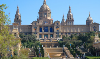 Vista del Palau Nacional de Barcelona con escalinatas, jardines verdes y turistas paseando alrededor.