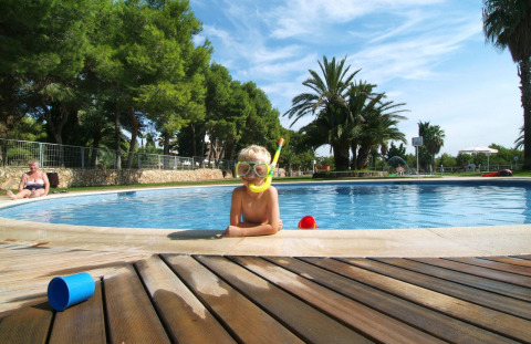 Bambino con attrezzatura da snorkeling in piscina al Camping Vilanova Park, Catalogna, circondato da palme.