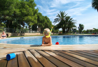 Bambino con attrezzatura da snorkeling in piscina al Camping Vilanova Park, Catalogna, circondato da palme.