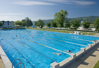 Piscina al aire libre con carriles y nadadores en Camping Terme Catez, rodeada de árboles y colinas, Eslovenia.
