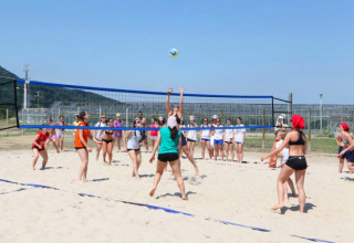 Teens play beach volleyball at Camping Terme Catez holiday park in Slovenia, watched by a group nearby.