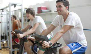 Dos hombres jóvenes usan bicicletas estáticas y sonríen en el gimnasio de Camping Terme Catez en Eslovenia.