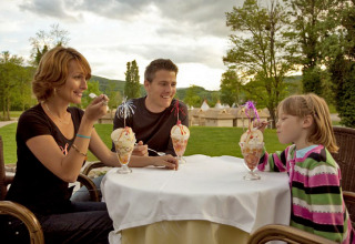 A family enjoys ice cream sundaes outdoors at Camping Terme Catez in Slovenia, surrounded by green scenery.