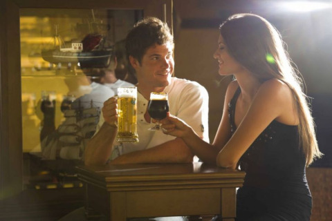 A young couple enjoys beers together at a bar in Camping Terme Catez, Lower Sava, Slovenia, smiling warmly.