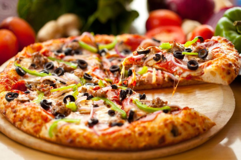 Pizza recién horneada con aceitunas negras, pimientos verdes y queso en bandeja de madera en Camping Terme Catez, Eslovenia.