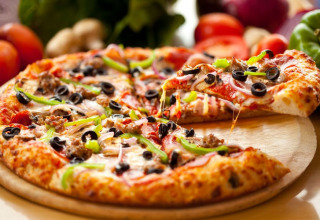 Freshly baked pizza with black olives, green peppers, cheese on a wooden tray at Camping Terme Catez in Slovenia.
