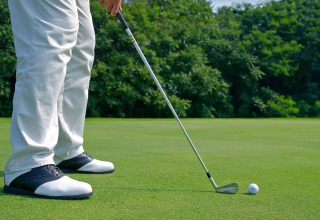 A golfer in white pants and black shoes prepares to putt a ball on a green course near Brežice, Slovenia.