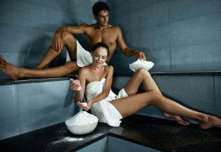 Couple enjoys steam bath at Camping Terme Catez, Slovenia, wearing towels and applying mineral mud.