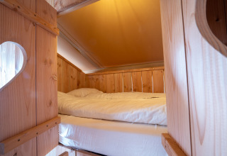 Cama acogedora en tienda safari SunLodge Pamoja&Kambi en Camping Terme Catez, Eslovenia, con decoración de madera.