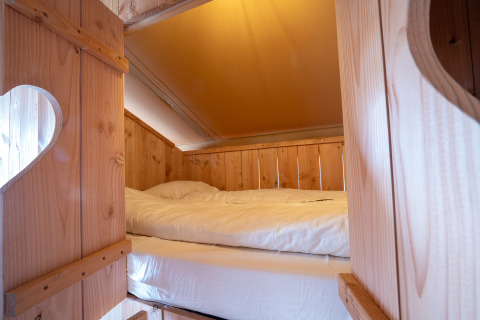 Cama acogedora en tienda safari SunLodge Pamoja&Kambi en Camping Terme Catez, Eslovenia, con decoración de madera.