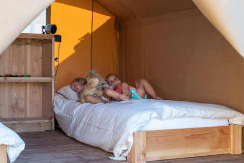 Dos niños descansan en una cama dentro de una tienda safari en SunLodge Pamoja & Kambi, Camping Terme Catez, Eslovenia.
