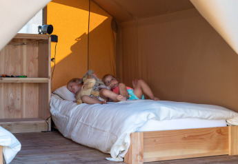 Twee kinderen rusten op een bed in een safaritent bij SunLodge Pamoja & Kambi, Camping Terme Catez, Slovenië.