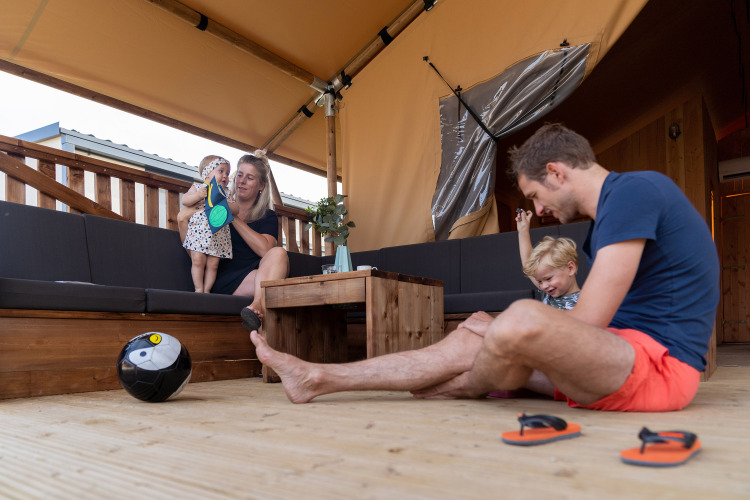 Familia relajándose en una tienda SunLodge Taiga en Camping Terme Catez, Eslovenia, niños jugando balón.