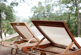 Two wooden sun loungers at SunLodge Jungle safari tent in Camping Vilanova Park, Spain, surrounded by trees.