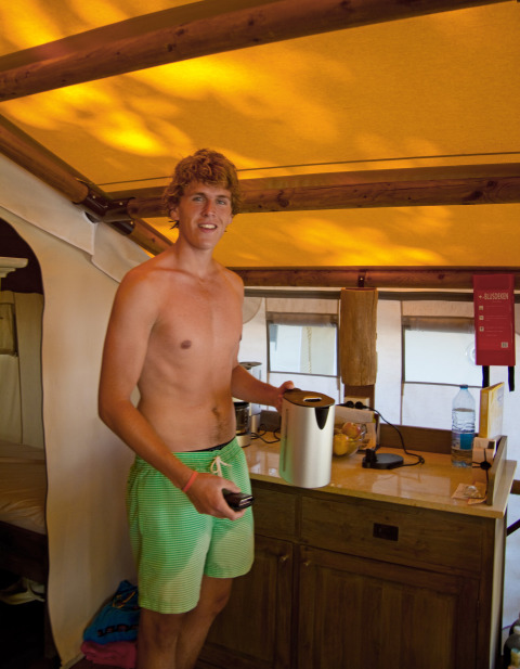 Joven con bañador verde está sin camiseta en una tienda safari SunLodge Jungle en Camping Vilanova Park, España.