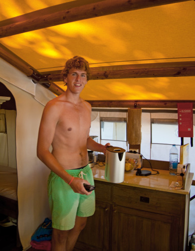 Joven con bañador verde está sin camiseta en una tienda safari SunLodge Jungle en Camping Vilanova Park, España.