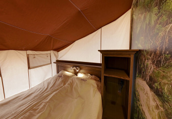 Vista interior de la tienda safari SunLodge Jungle con cama doble y estantería en Camping Vilanova Park, España.