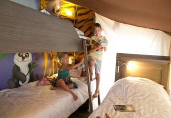 Bambini che giocano e leggono in una tenda safari a tema giungla presso SunLodge Jungle, Camping Vilanova Park, Spagna.