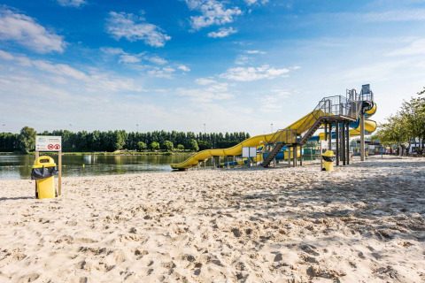 Beach with yellow water slide by the lake at Vakantiepark Klein Strand, a holiday park in West Flanders, Belgium.