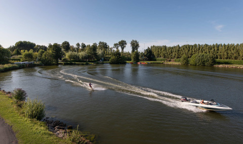 Wasserskifahrer wird von einem Motorboot auf einem ruhigen See im Vakantiepark Klein Strand, Belgien gezogen.